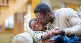 Father giving his son a kiss on the cheek while sitting on a couch
